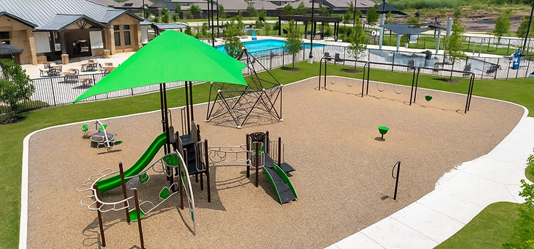 Community playground with climbing structures, slides, swings, and shade canopy.